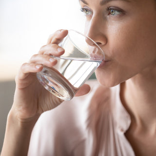 Frau trinkt HEPY Bitter BIO-Tropfen verdünnt in einem Glas Wasser