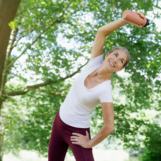Lachende Frau beim Stretching im Freien mit einer Hantel im grünen Park