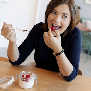 Frau mit Himbeeren und Joghurt-Dessert in heller Küche
