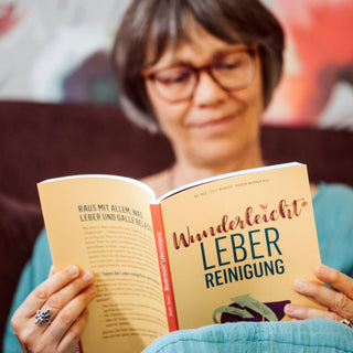 Frau liest das Buch Wunderleicht Leberreinigung mit gelbem Cover auf einem Sofa