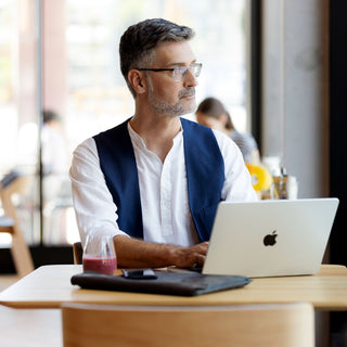 Mann mit Brille arbeitet am Laptop im Cafe mit einem Smoothie-Glas auf dem Tisch