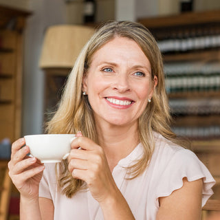 Lächelnde Frau hält weiße Teetasse in einem Teegeschäft – Wohlfühl-Porträt-Bild für HEPY Kaffee BIO